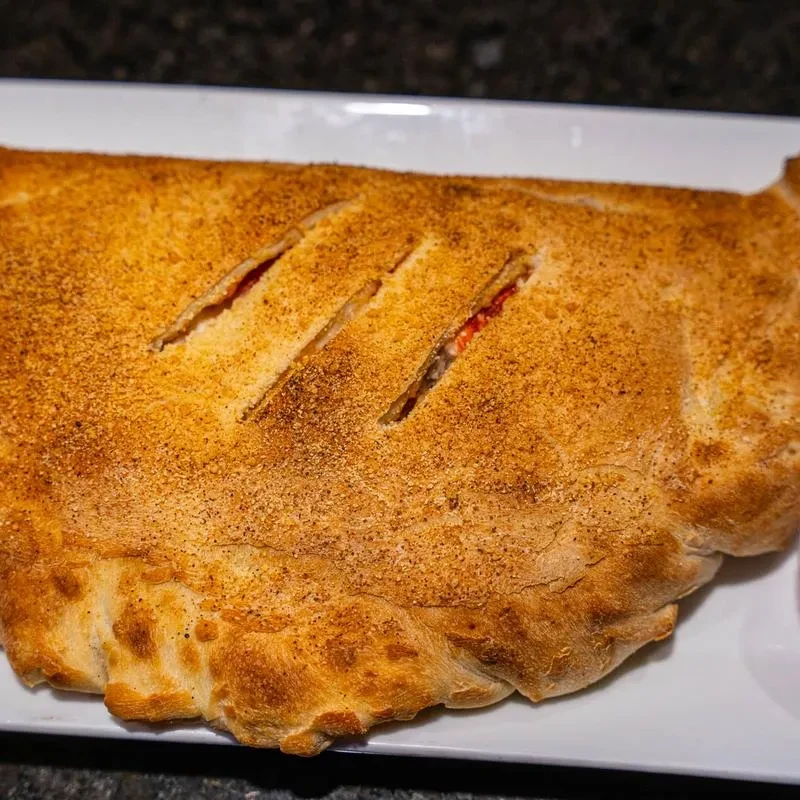 Golden-brown baked pastry, slits reveal reddish filling, on white plate.