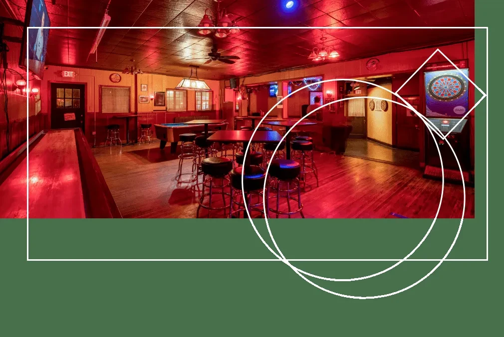 Red-lit bar interior with tables, shuffleboard, pool table, and dartboard.