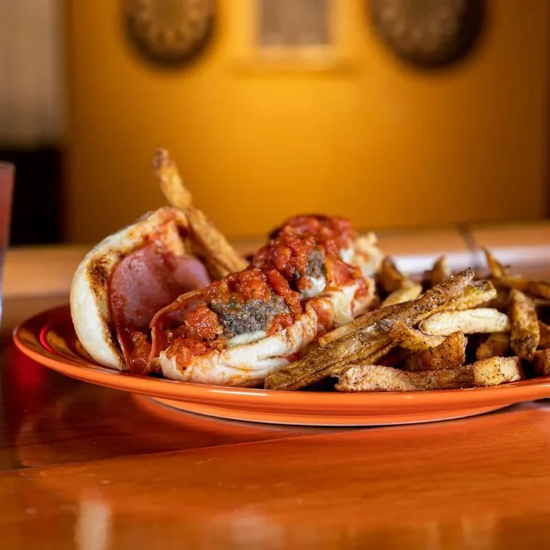 Meatball sub, sausage, and fries on an orange plate.
