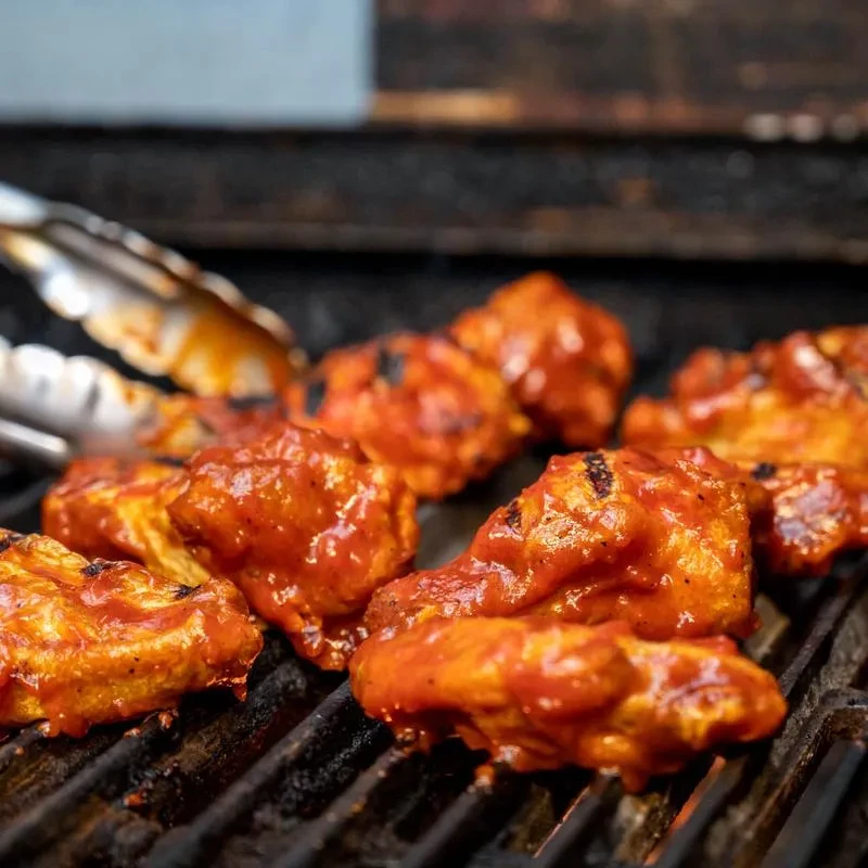 Several sauced chicken wings grilling on a metal grate with tongs.
