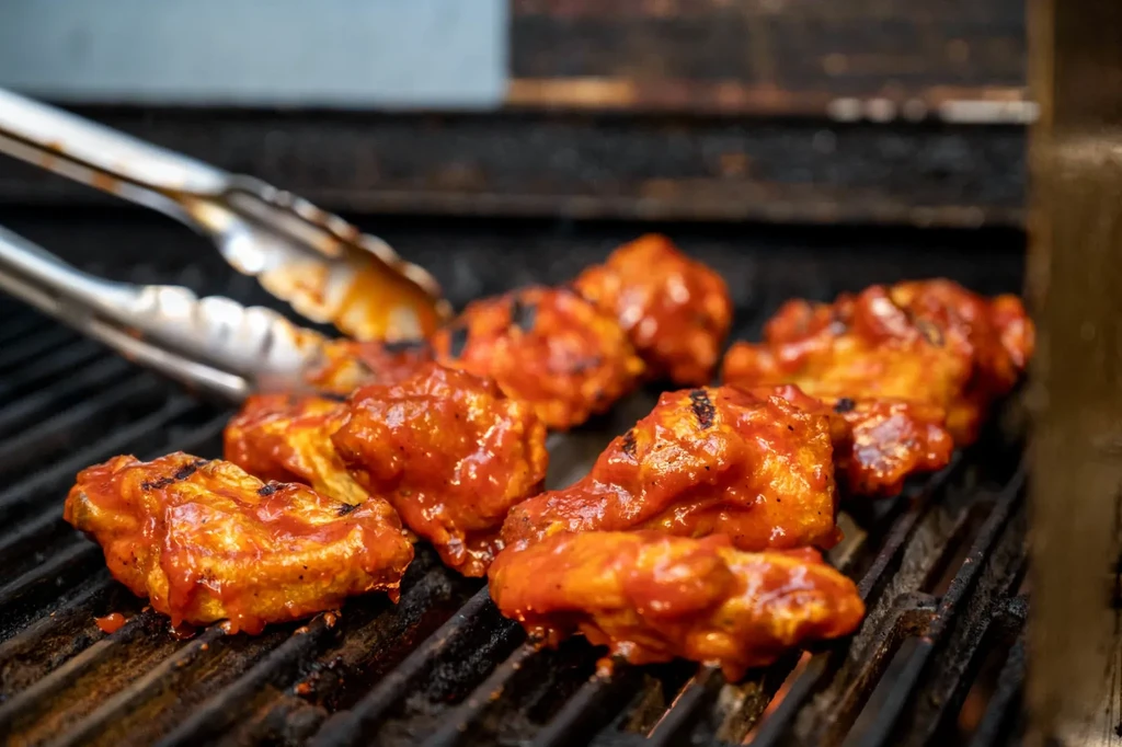 Reddish-orange sauced chicken wings with char marks grilling on a grate.
