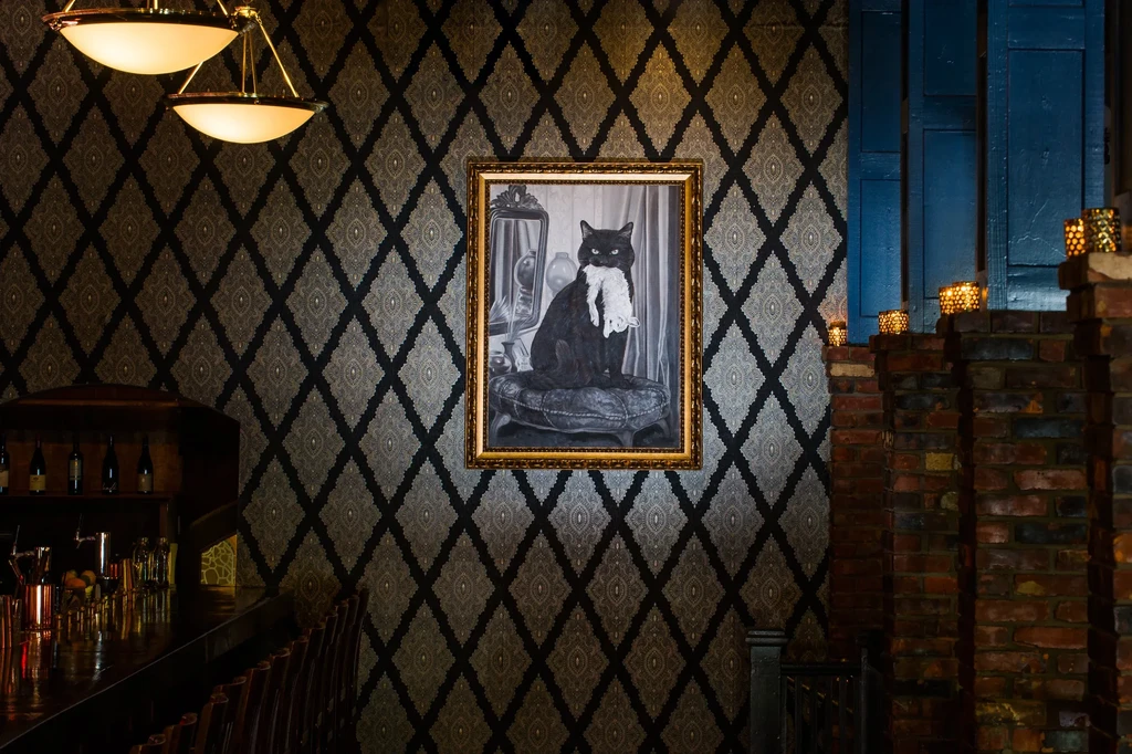 Ornate gold-framed black cat painting on dark wallpaper in a bar.