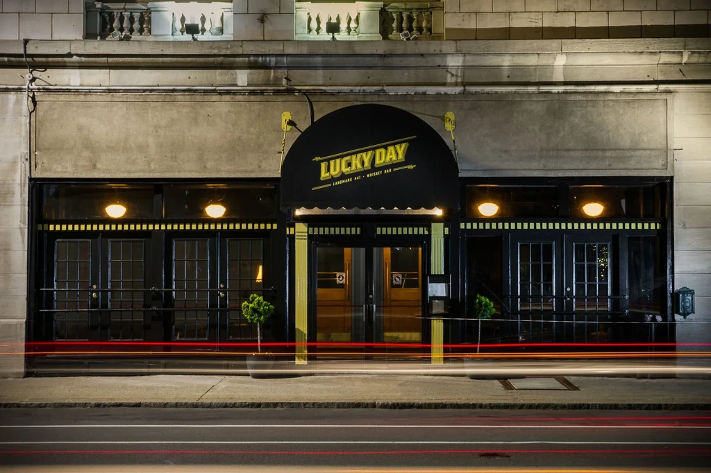 "Lucky Day" whiskey bar storefront illuminated at night, urban scene.