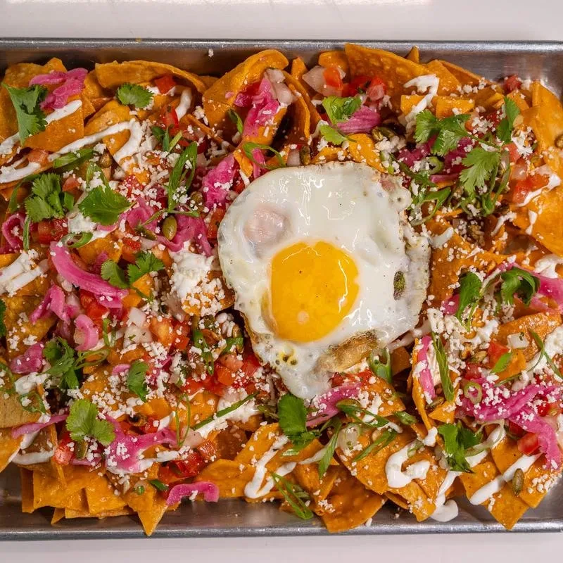Loaded nachos with a runny fried egg, cheese, tomatoes, and crema.