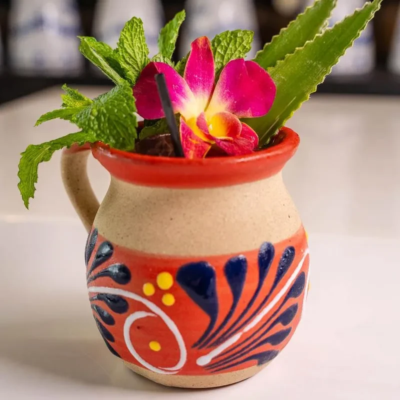 Handcrafted ceramic folk art mug holding an elaborately garnished drink.