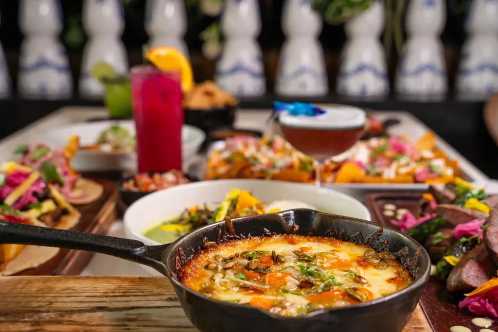 Close-up of a restaurant table with cheesy dish, tacos, and cocktails.