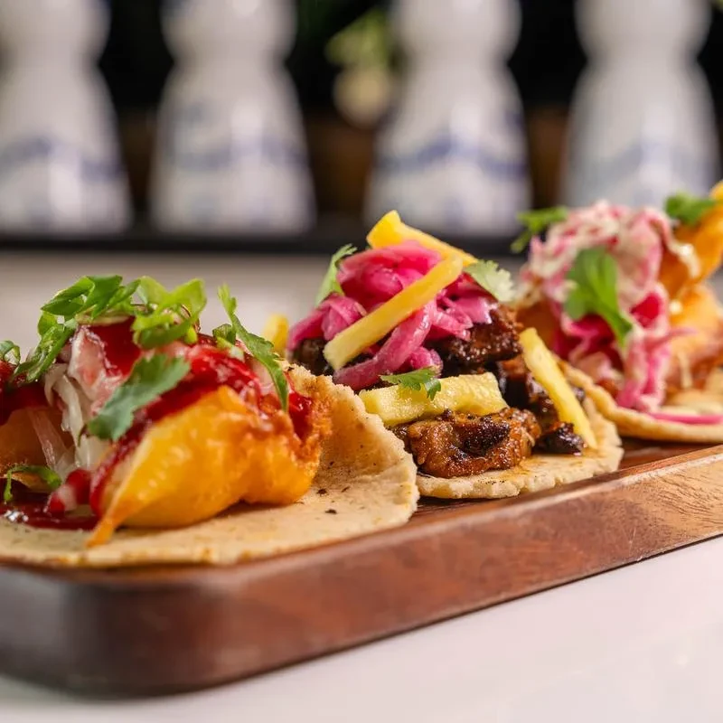 Three vibrantly colored tacos on a dark wooden serving board.