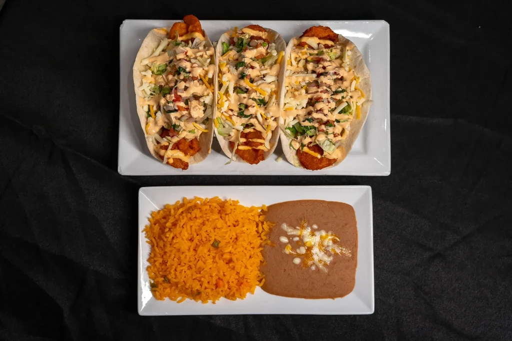 Three tacos, Mexican rice, and refried beans on plates.