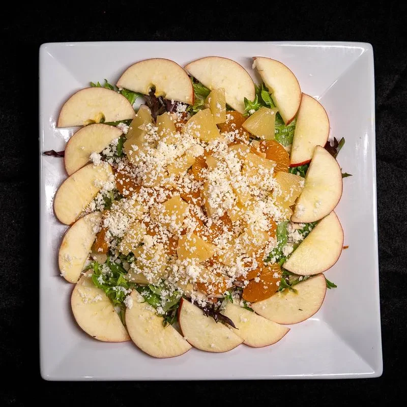 Colorful salad with mixed greens, apples, pineapple, oranges, and crumbled cheese.