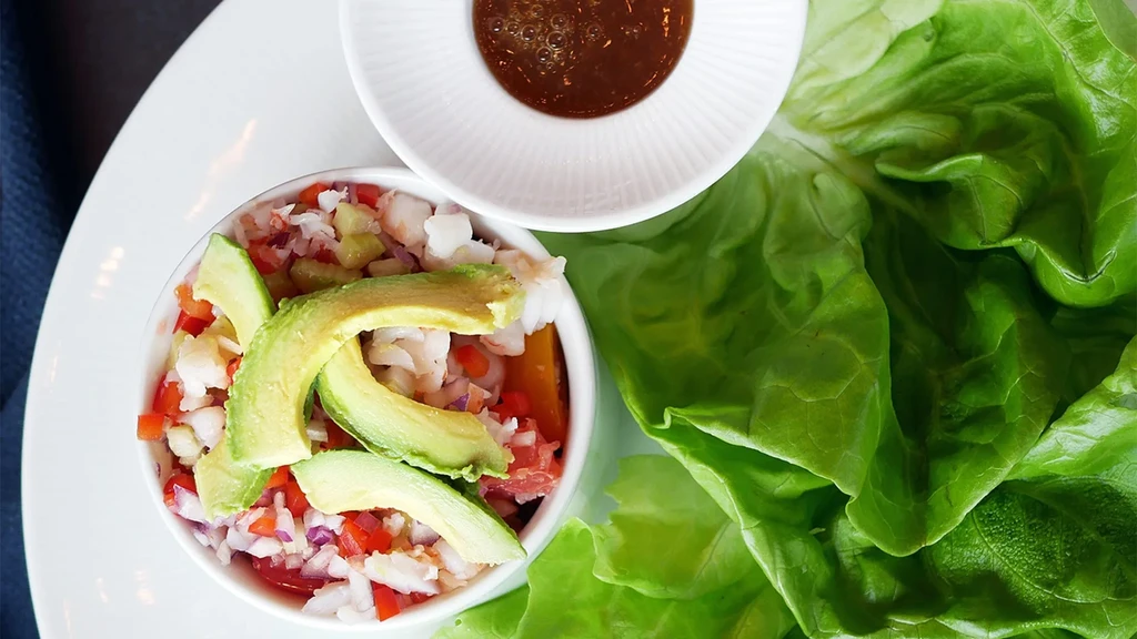 Fresh ceviche bowl with seafood, diced vegetables, avocado, lettuce, and sauce.