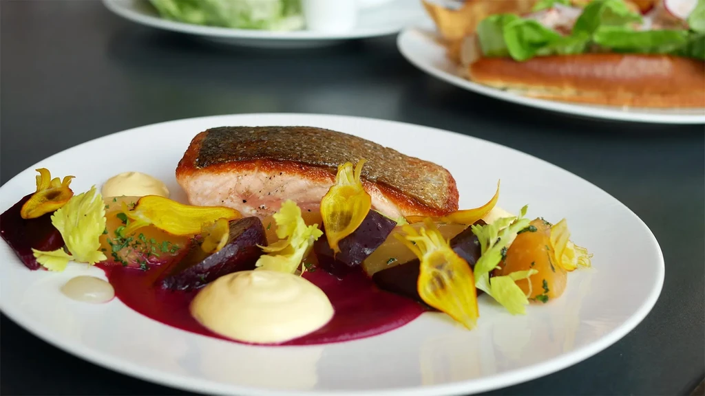 Meticulously plated pan-seared salmon with colorful vegetables and sauces.