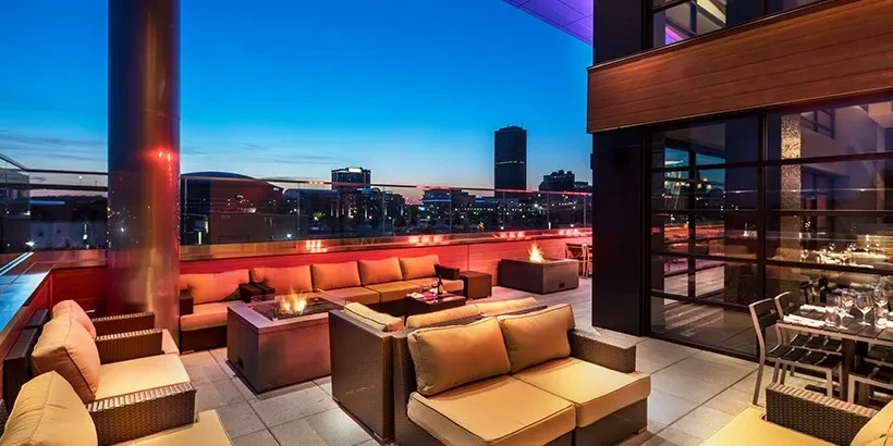 Modern rooftop terrace with lounge seating, fire pits, and city view.