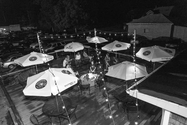 Overhead black and white patio with people, string lights, and fire pit.