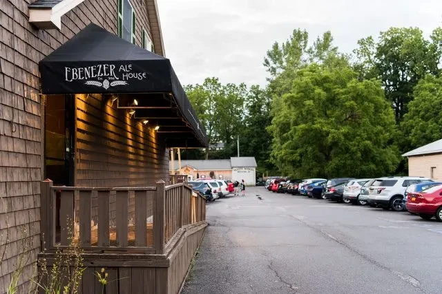 Ebenezer Ale House: rustic wooden exterior, lighted awning, large parking lot.