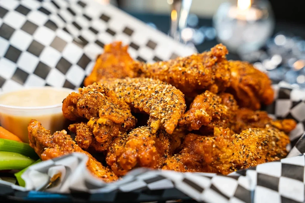 Basket of seasoned fried chicken wings with sauce, celery, and carrots.