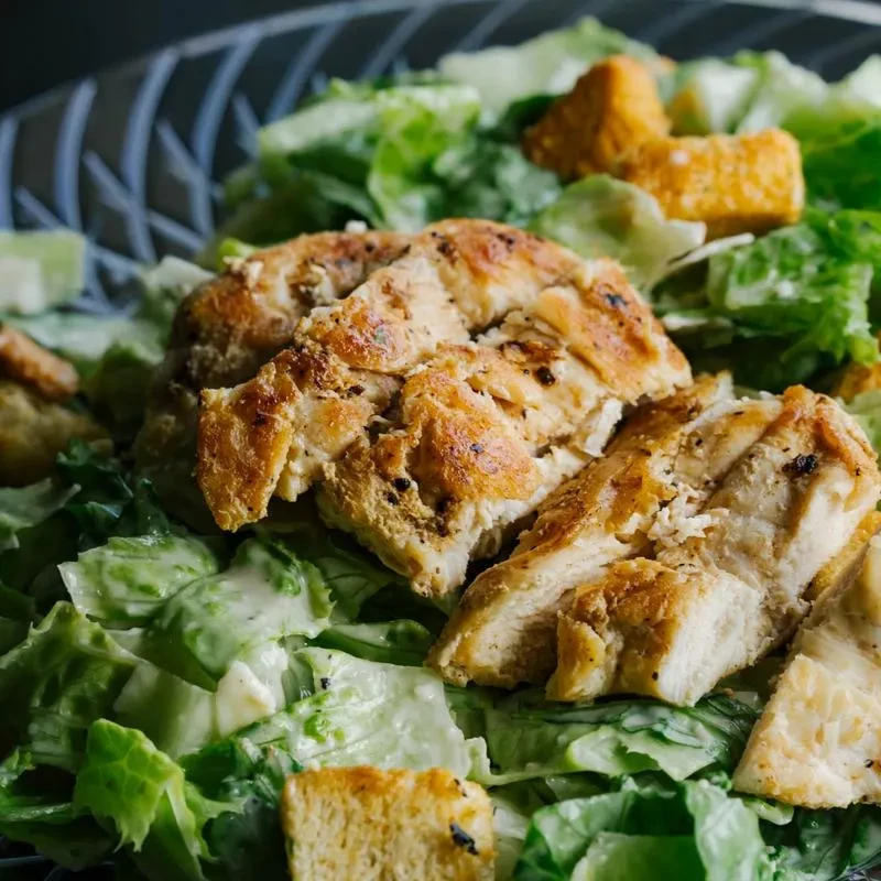 Close-up top-down Caesar salad with grilled chicken and croutons.