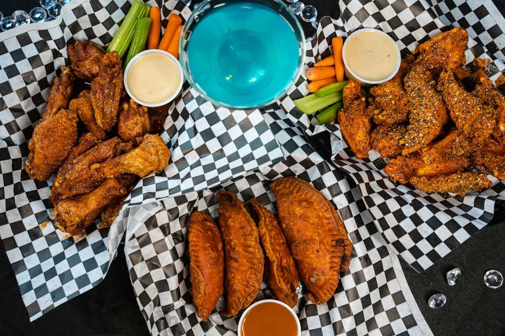 Overhead view of chicken wings, pastries, sauces, and a blue drink.