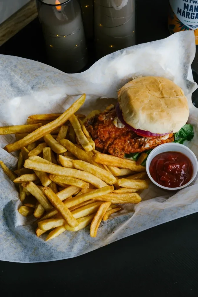 Close-up of a fried chicken sandwich, fries, and ketchup with warm lighting.