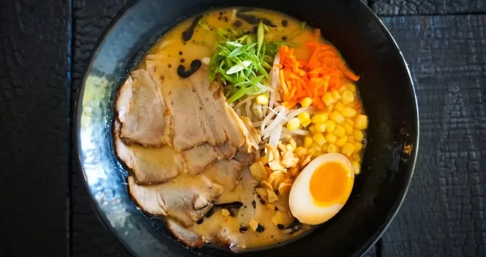 Top-down ramen with pork, soft egg, scallions, carrots, and corn.