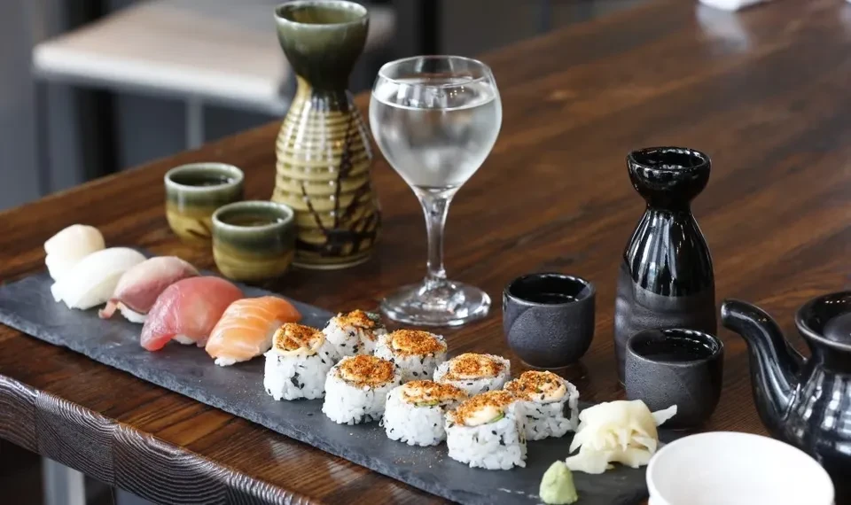 A slate platter of nigiri and maki sushi with sake and tea.