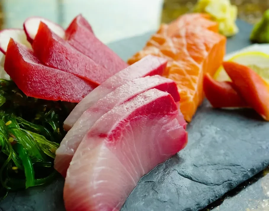 Close-up of assorted sashimi, including tuna and salmon, on a slate board.
