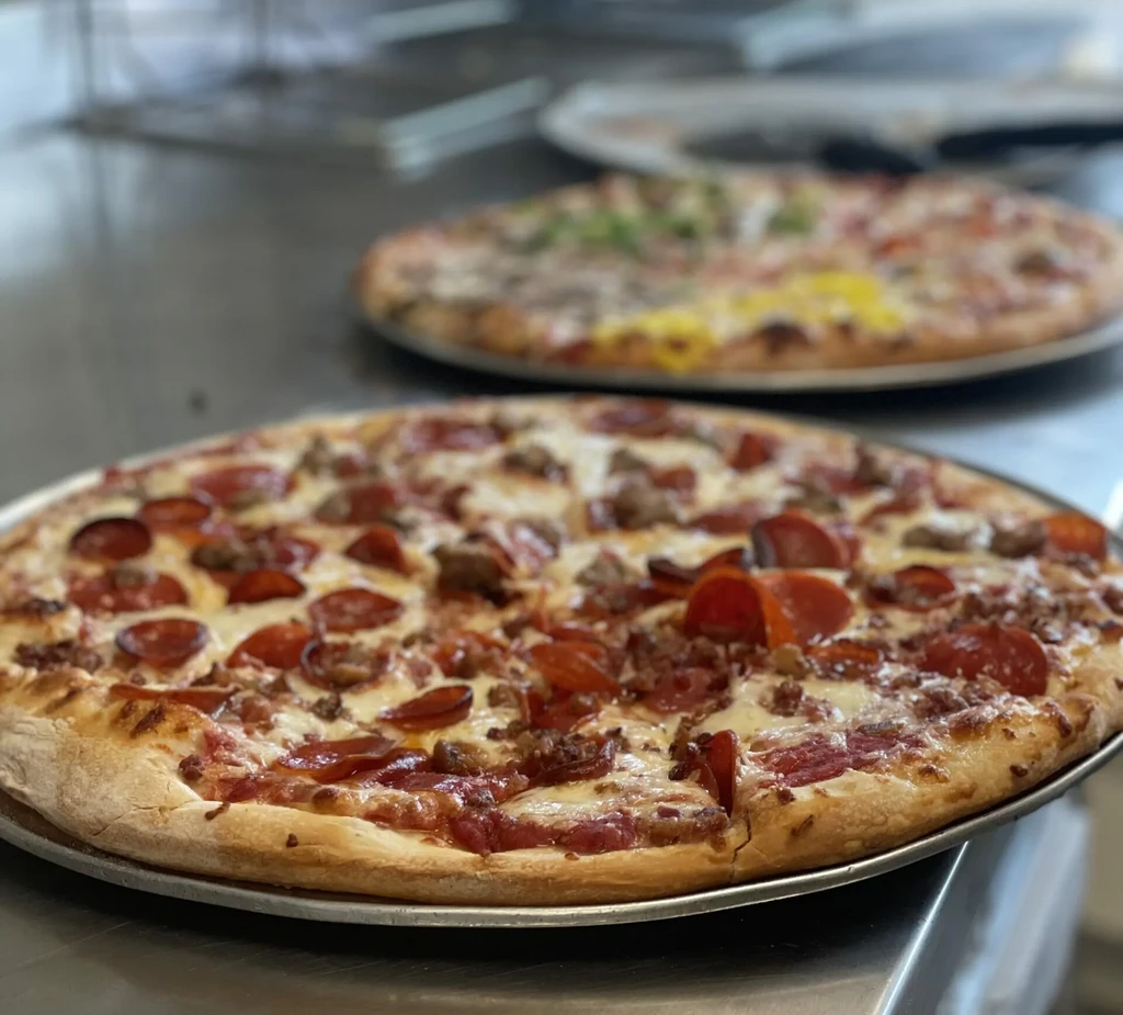 Two pizzas on metal trays, one pepperoni and sausage with cut slice.