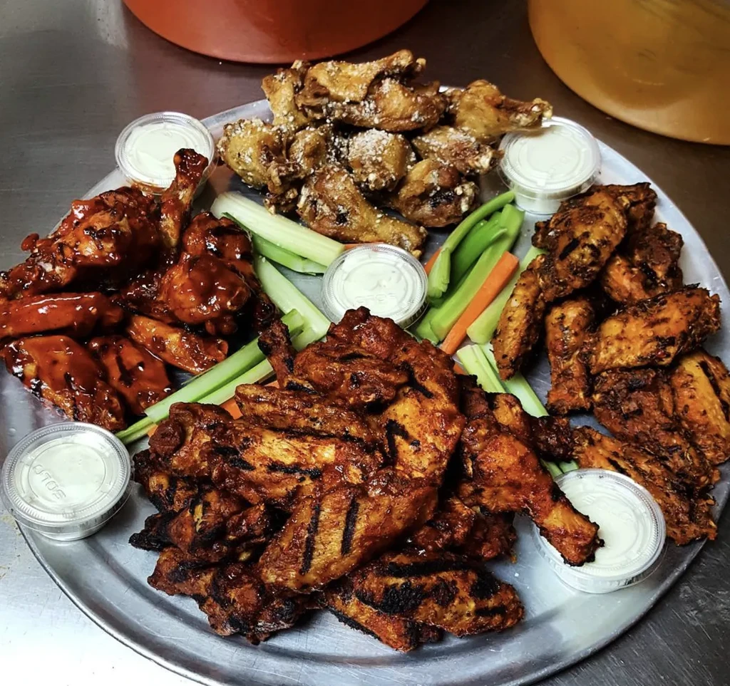 Platter of four distinct chicken wing preparations, vegetables, and dips.
