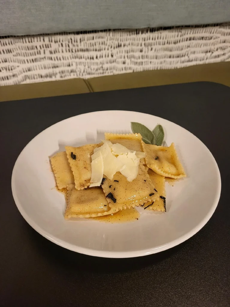 White plate of golden pasta with sauce, Parmesan, and sage leaves.