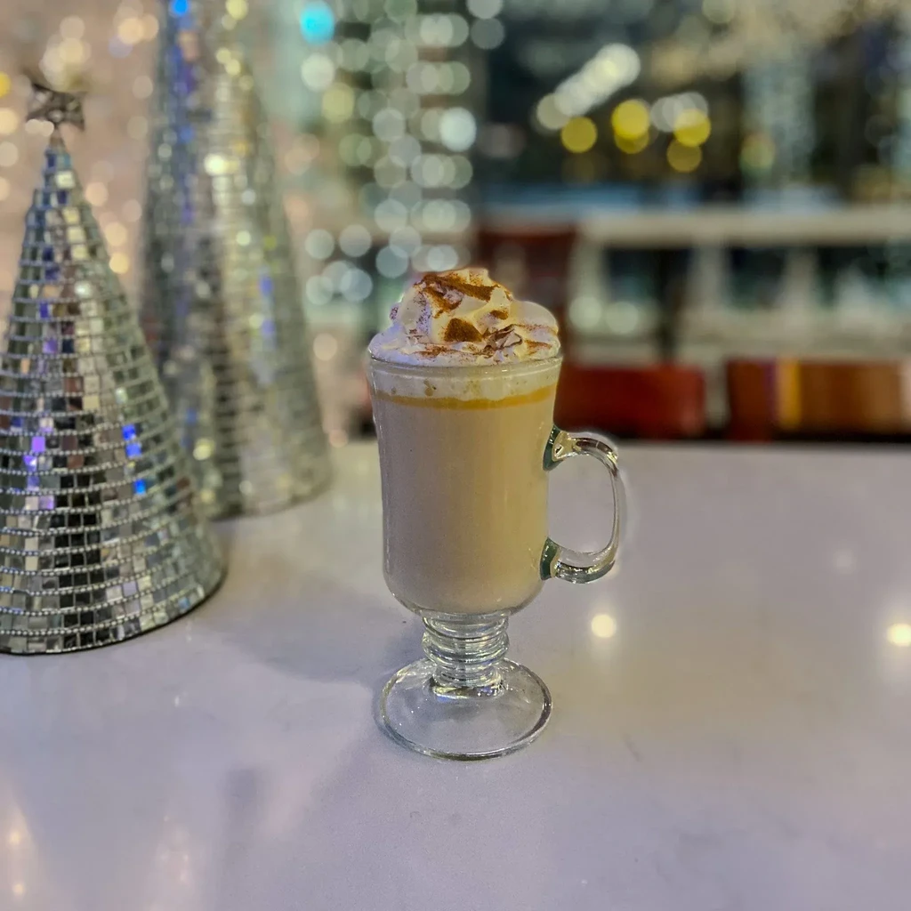 Festive caramel drink with whipped cream, cinnamon, and holiday decorations.