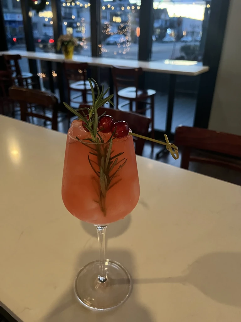 Pink cocktail in a stemmed glass, garnished with rosemary and cranberries.