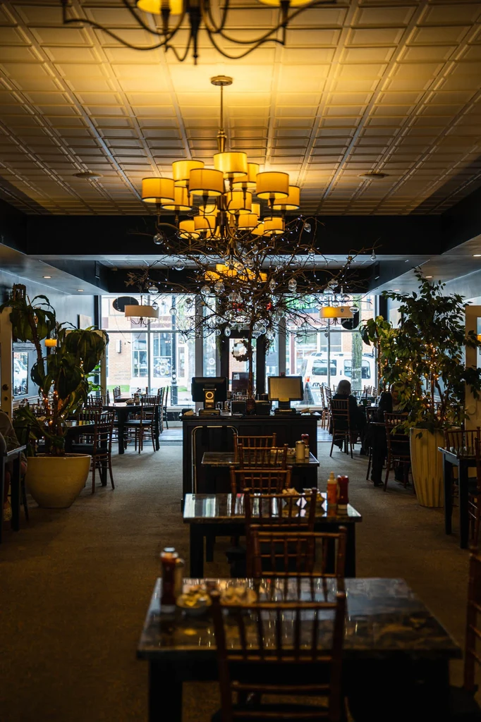 Warmly lit, elegant restaurant with prominent chandelier, tree decor, and tables.