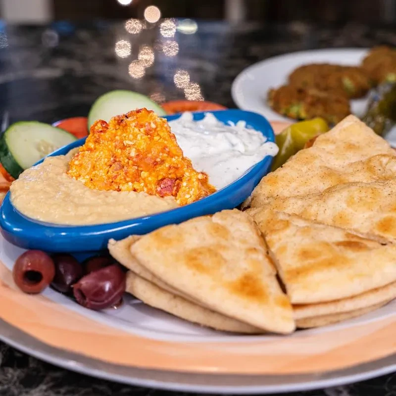 Mediterranean appetizers: hummus, two dips, pita, olives, vegetables.
