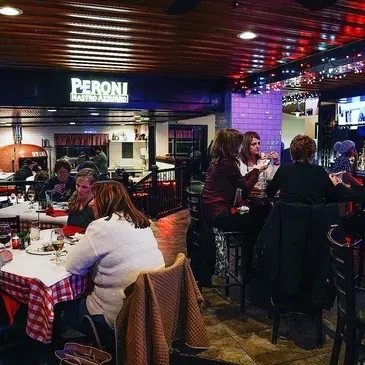 Warmly lit Peroni Gastro Abruzzo restaurant with diners and brick oven.