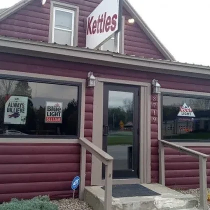 Kettles bar exterior with reddish-brown siding, large windows, and promotional signs.