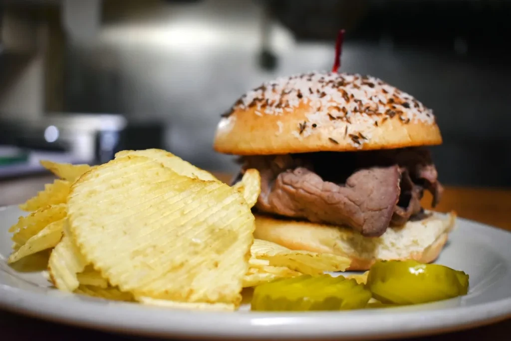 A roast beef sandwich, ridged chips, and dill pickles on a plate.