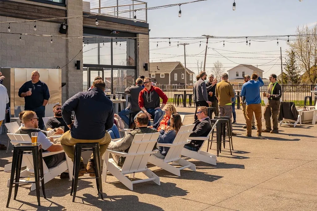 People socialize and drink on a sunny outdoor patio with string lights.