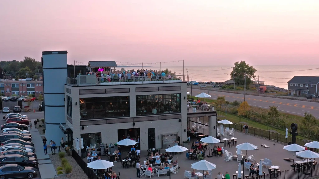 Aerial view: busy multi-level restaurant with patios by water at dusk.