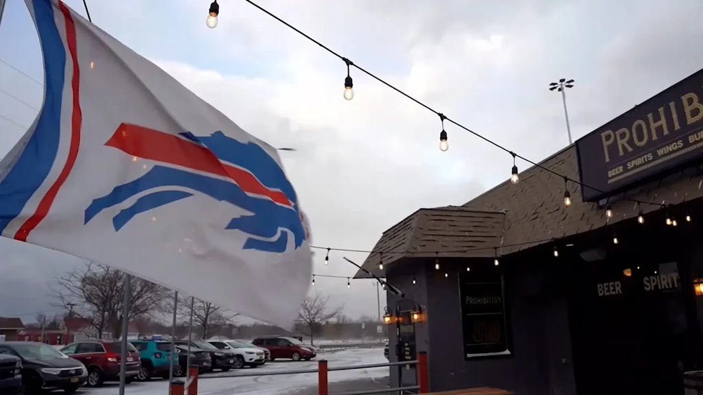 Buffalo Bills flag in snow outside Prohibition bar with string lights.