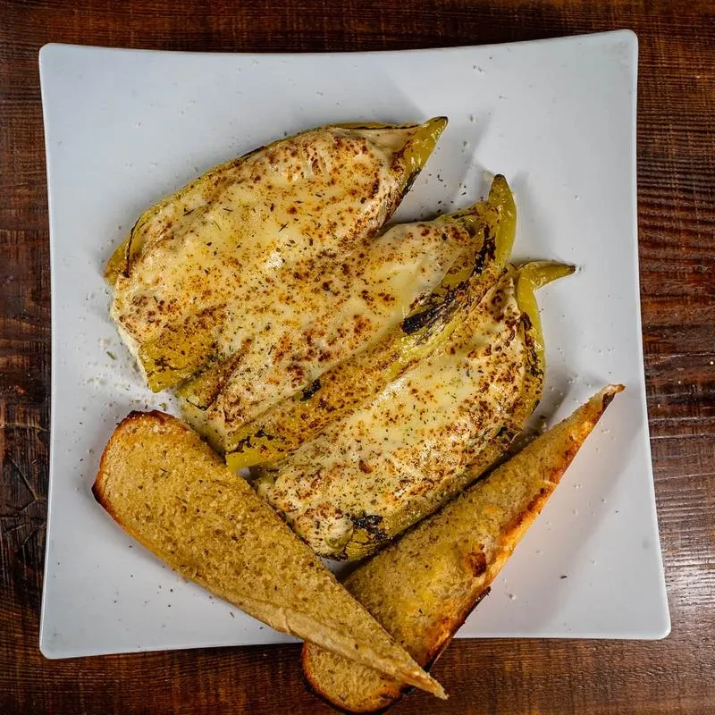Three roasted peppers topped with cheese, served with toasted bread.