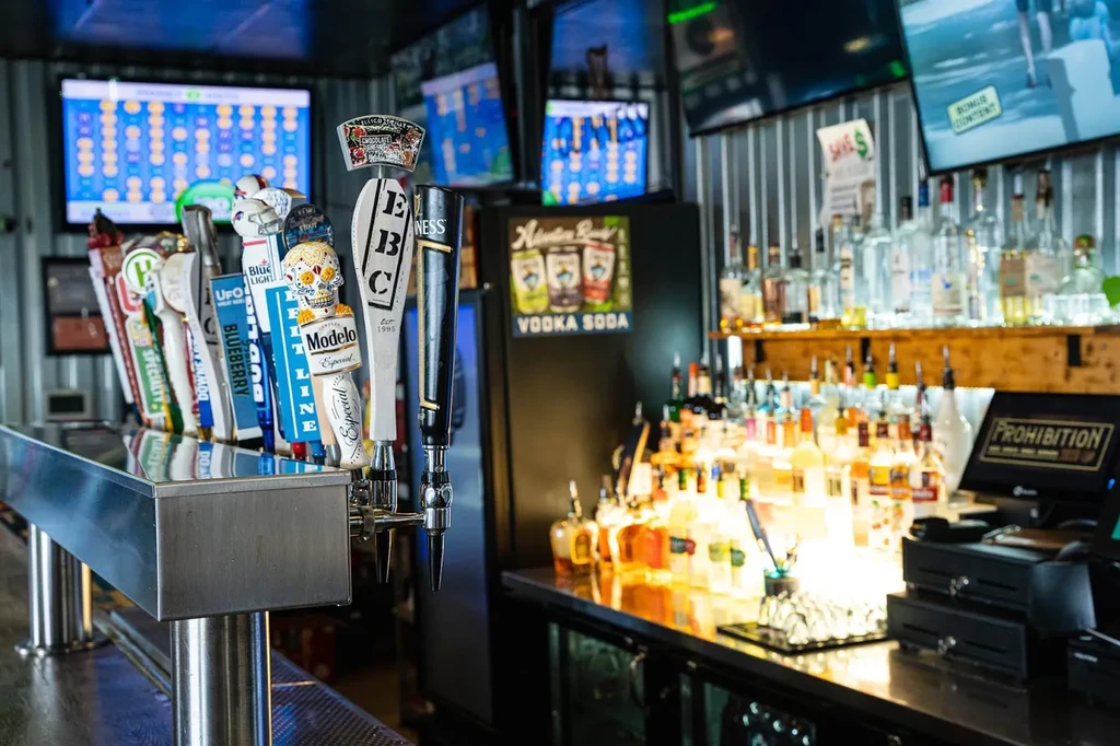 Modern bar with beer taps, glowing liquor bottles, and sports televisions.
