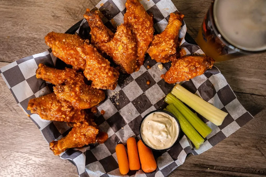 Buffalo chicken wings with dip, carrots, celery, beer on a wooden table.
