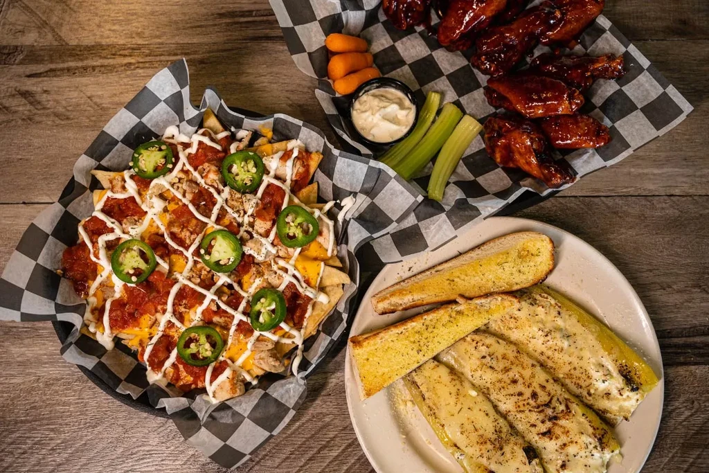 Overhead shot: nachos, wings, zucchini, and garlic bread on a table.