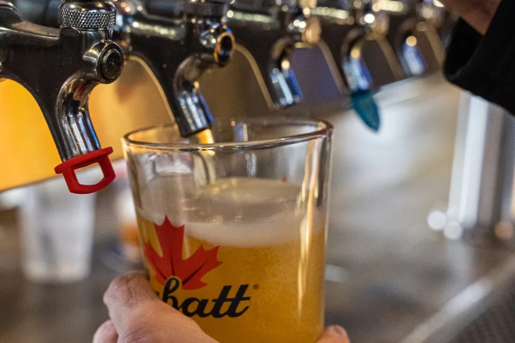 Hand holds a Labatt beer glass being filled from a chrome tap.
