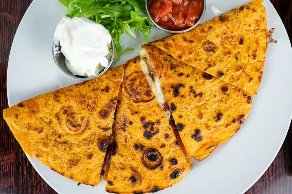 Cooked quesadilla cut into slices, with salsa, sour cream, and lettuce.