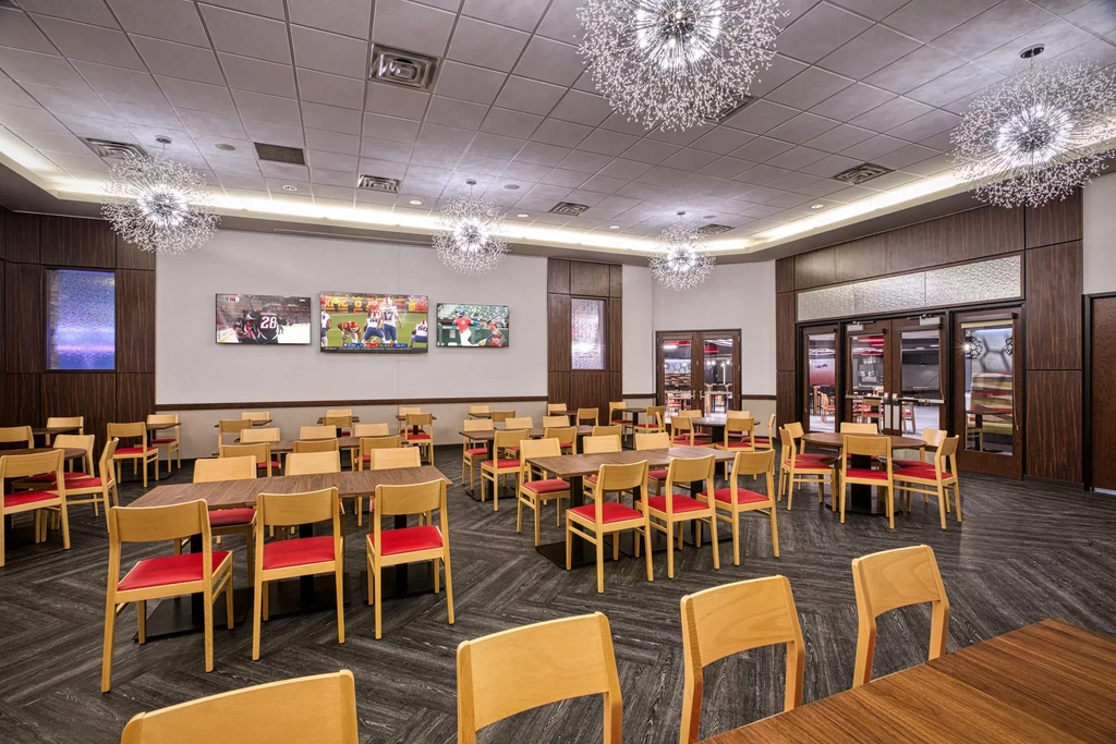 Modern empty restaurant with red chairs, starburst lights, and sports TVs.