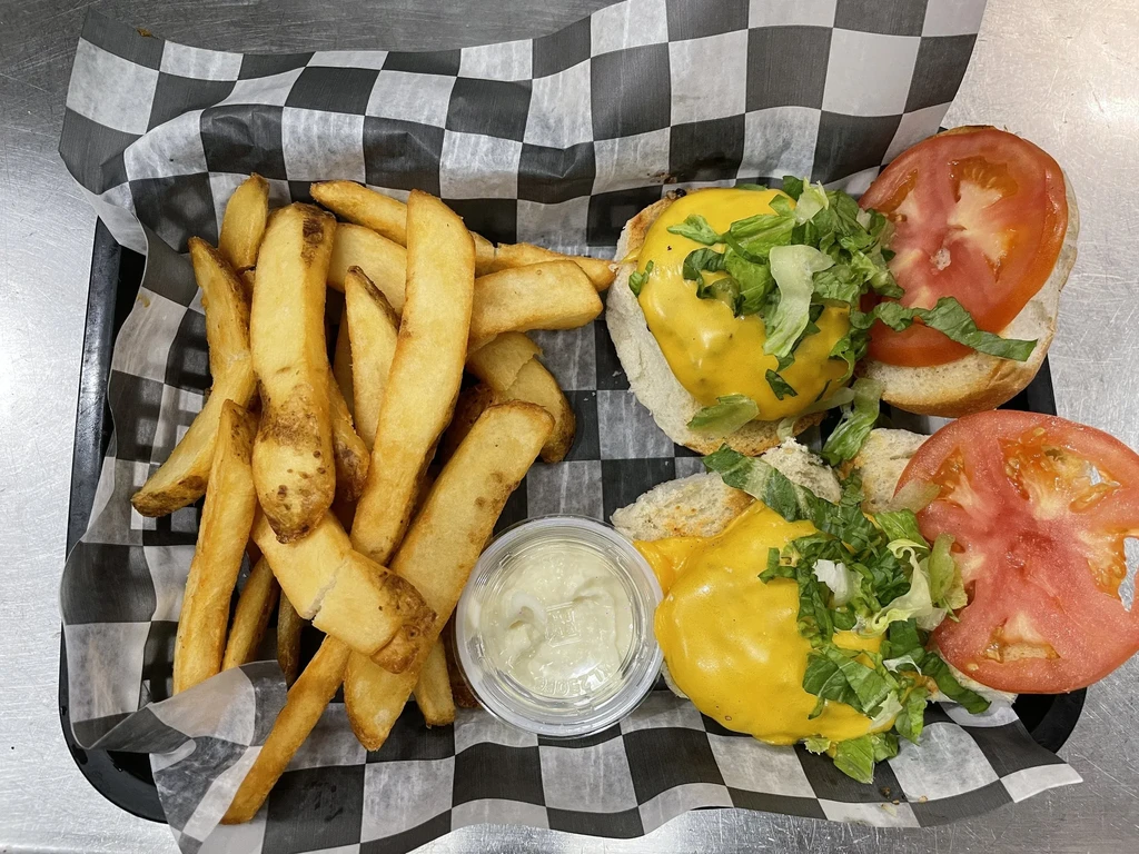 Two mini cheeseburgers, golden wedge fries, and sauce in a basket.