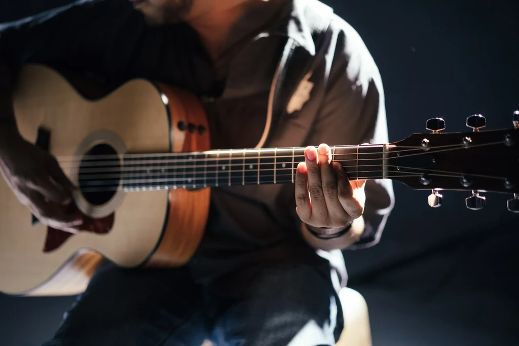 Close-up of hands playing a two-tone acoustic guitar, dramatically lit.