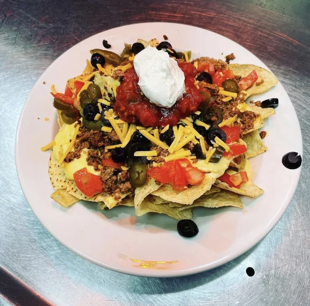 Nachos piled high with meat, cheese, vegetables, salsa, sour cream.