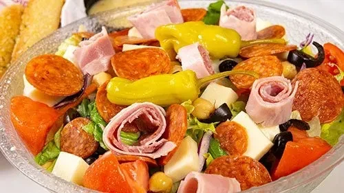 Colorful antipasto salad in a clear bowl with pepperoni, ham, cheese, peppers.