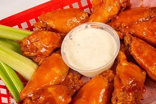 Buffalo chicken wings, celery, and dip in a red basket.